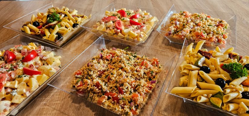 Assortiment de salades de pâtes colorées dans des plats transparents.